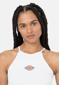 Hvit singlet med en tettsittende design som har en fargerik "Dickies"-logo på brystet og tynne stropper. Glatt tekstur med minimale utsmykninger.