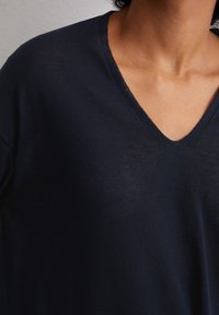 Top scuro navy a V realizzato in un tessuto leggero e morbido. Il scollo presenta una sottile texture a coste, offrendo una vestibilità rilassata.