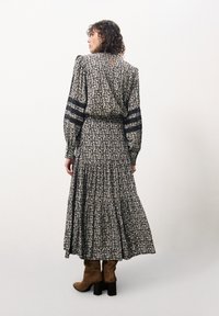 Lang zwart jurkje met crèmekleurig bloemenpatroon, gezwollen mouwen, een getailleerde taille, een gelaagde rok en een keyhole-detail op de rug. Gestyled met bruin kniehoge laarzen.