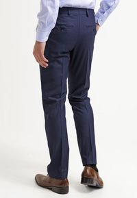 Navy tailored trousers with a smooth texture, slim fit, and two back pockets; paired with brown dress shoes.