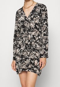 Black wrap dress with long sleeves, featuring a beige and pink floral pattern. Made of lightweight fabric, with a tie at the waist.