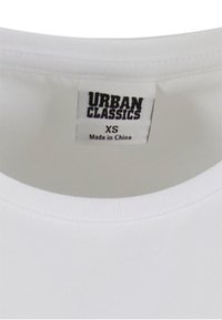 Encolure de t-shirt blanche avec une étiquette indiquant Urban Classics, taille XS, fabriqué en Chine.