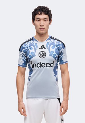 Man draagt lichtgrijs voetbalshirt met blauwe bloemenpatronen, zwarte Adidas- en Eintracht Frankfurt-logo's en de sponsortekst "indeed".