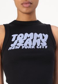 Svart erméløs topp med ribbestruktur, med fet hvit grafisk tekst: "TOMMY JEANS NEW YORK CITY" over brystet.