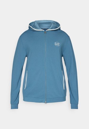 Sweat à capuche zippé bleu avec cordon de serrage, présentant des accents blancs, des poches latérales et un petit logo de marque sur la poitrine.