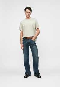 Beige cotton t-shirt with short sleeves, paired with dark blue flared denim jeans and a brown leather belt. Black shoes complete the outfit.