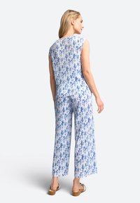 Zweiteiliges Outfit mit einem ärmellosen, blauen Oberteil mit floralem Muster und weit geschnittenen Hosen aus einem leichten, strukturierten Stoff.