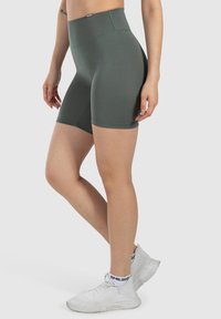 Szorty sportowe o wysokim stanie w ciemnozielonym kolorze, wykonane z elastycznego materiału, charakteryzujące się gładką teksturą i dopasowanym krojem, kończące się powyżej kolana.