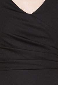 Schwarzer Kleidungsstoff mit einer weichen Textur, der einen V-Ausschnitt und ein ausgefeiltes Wickeldesign an der Brust aufweist, um eine figurbetonte Silhouette zu schaffen.