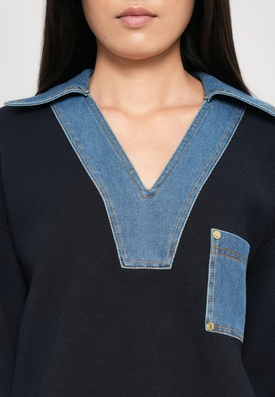 Maglione nero con dettagli in denim; presenta un ampio scollo a V, un colletto in denim a contrasto e una tasca con dettagli in oro.