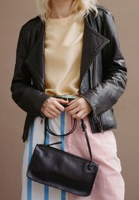 Czarna skórzana torba na ramię o gładkiej fakturze, z cienkim paskiem i prostokątnym kształtem. Dopasowana do żółtej bluzki i spódnicy w paski.