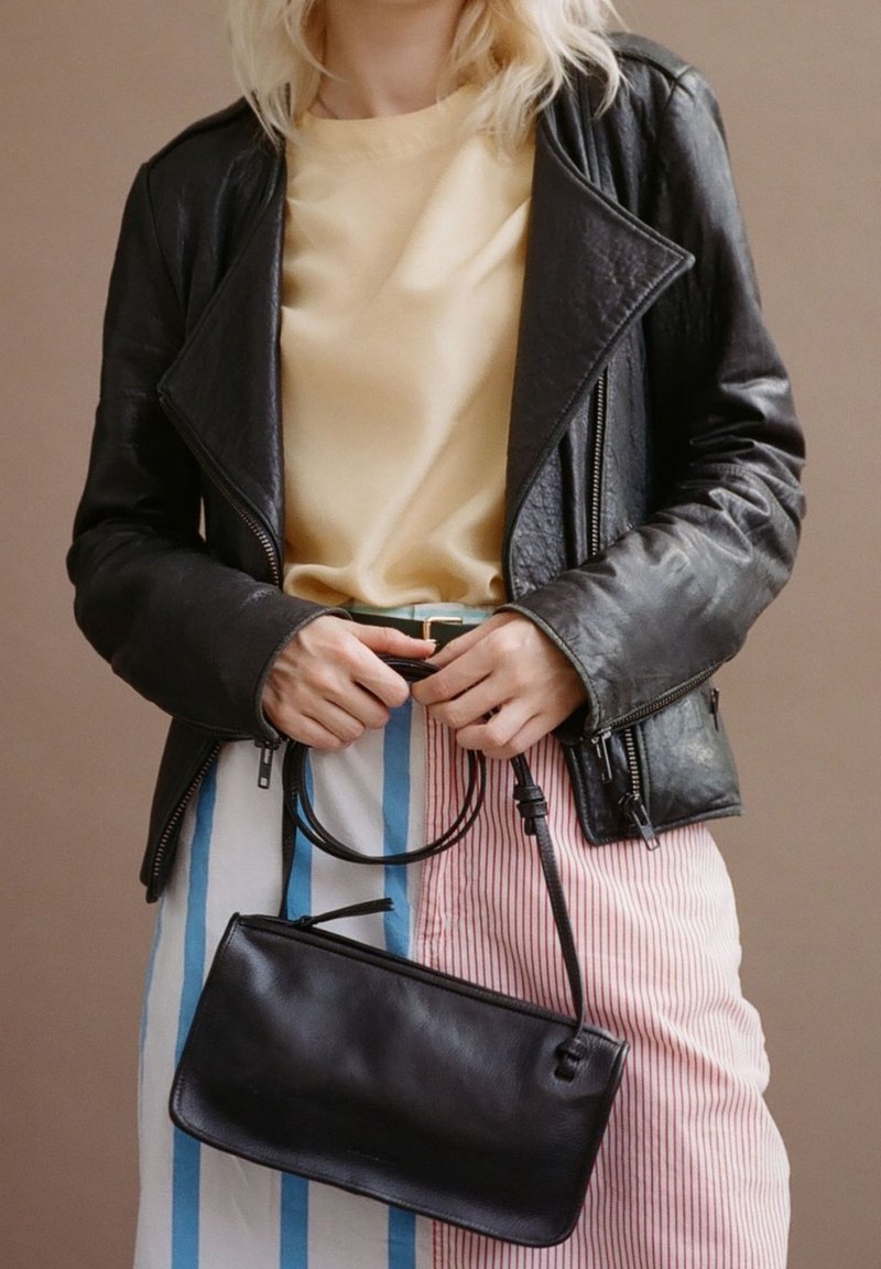 Czarna skórzana torba na ramię o gładkiej fakturze, z cienkim paskiem i prostokątnym kształtem. Dopasowana do żółtej bluzki i spódnicy w paski.