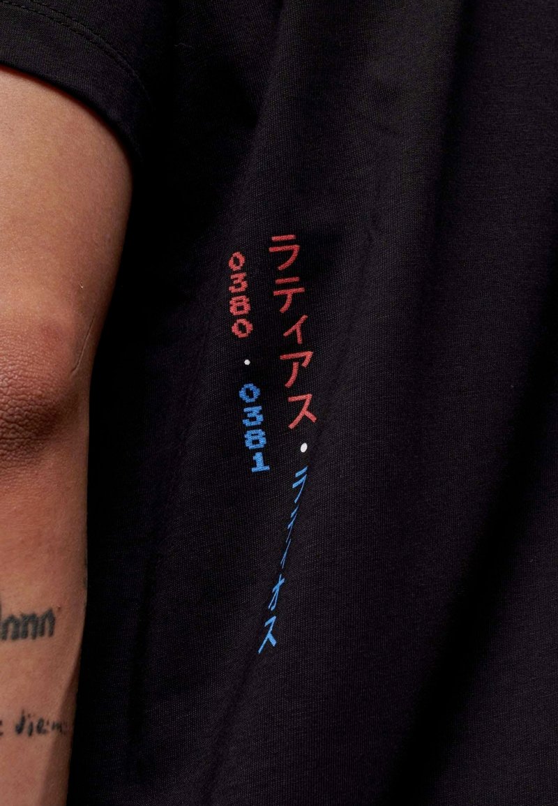 Zwarte katoenen T-shirt met multi-kleurige tekst in rood en blauw, met Japanse karakters en cijfers langs de mouw. Glad textuur.