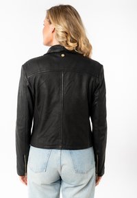 Zwarte leren jas met een getailleerd ontwerp, voorzien van een opstaande kraag, zichtbare stiksels en ritsmanchetten. Soepele textuur met minimale accenten.