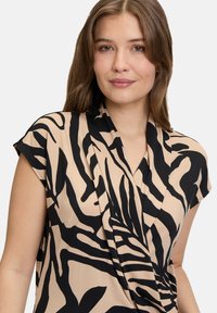 Blusa beige con strisce zebrate nere, maniche corte e frontale drappeggiato. Realizzata in tessuto morbido, presenta una scollatura a V e un design fluido.