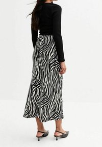 Černý žebrovaný top s dlouhým rukávem v kombinaci s bílou sukní s výrazným černým zebrovaným potiskem. Sukně má volný střih a sahá do poloviny lýtek.