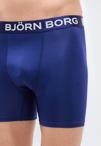 Μπλε μποξεράκια ναυτικού τόνου από λείο ύφασμα. Διαθέτουν λευκή ελαστική μέση με το λογότυπο "BJÖRN BORG". Σφιχτή εφαρμογή με τακτοποιημένα ράμματα.