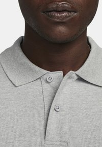 Harmaa polo-paita, joka on valmistettu teksturoidusta kankaasta, jossa on standardi kaulus, kaksi nappia ja siistit viimeistelyt reunoissa.