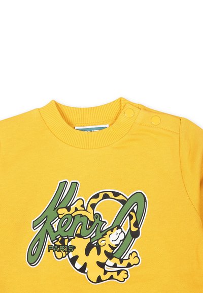 Sweat-shirt jaune avec un design graphique du texte vert "Kenzo Paris" accompagné d'une illustration de tigre ludique. Comprend des boutons-pression à l'épaule.