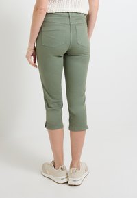 Pantalons cropped vert clair au design ajusté. Présente deux poches arrière et des fentes latérales à l'ourlet. Associés à des baskets beiges.
