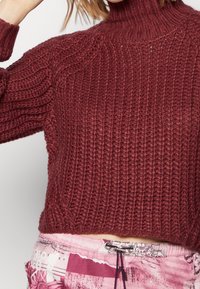 Ribbelgebreide trui in bordeauxrood, met een hoge hals en een cropped ontwerp. Textuurstof met een robuuste uitstraling, die een warme stijl toont.