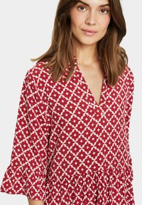 Röd och vit mönstrad blus med V-ringning, trekvartslånga ärmar med volangdetaljer och en halvt åtsittande bodice.