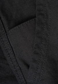 Black fabric with visible diagonal and parallel stitching, showing texture and a folded seam.