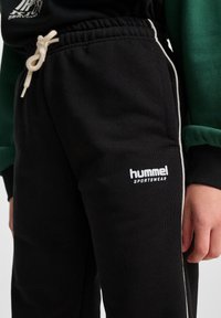 Czarne dresy z białymi paskami po bokach i z przodu z logo "hummel sportswear". Posiadają elastyczny pasek w talii z sznurkiem.