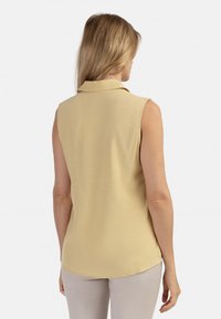 Mouwloze blouse in lichtgeel, met een kraag, een soepele textuur en een gebogen zoom. Ontworpen met een relaxte pasvorm voor comfort.