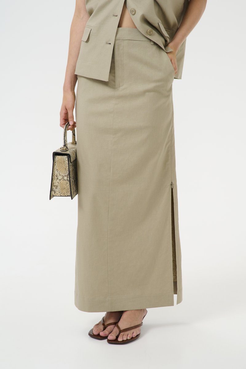 Gonna beige, lunga fino al ginocchio, in un tessuto testurizzato con una fessura laterale e un taglio elegante e aderente. Abbinata a una borsa a tracolla con stampa pitone e sandali.