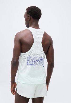 Mann, der ein weißes, perforiertes ärmelloses Sportoberteil mit lila Grafik und helle Laufshorts trägt, von hinten vor neutralem Hintergrund.