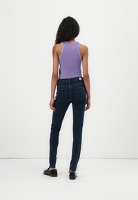 Purple ribbed tank top paired with dark blue skinny jeans. The outfit features a fitted design and a smooth texture, with minimal hardware.