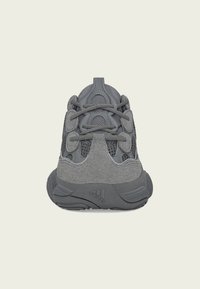 Sapatos atléticos cinzentos com uma mistura de materiais em malha e camurça, apresentando um design robusto com uma sola espessa e detalhes texturizados.