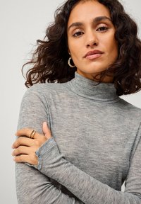 Grauer langärmeliger Rollkragenpullover aus weichem, strukturiertem Stoff. Mit Daumenlöchern für zusätzlichen Komfort und eine perfekte Passform, dazu eine figurbetonte Silhouette.