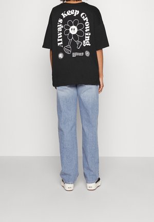 Czarny, oversize'owy t-shirt z białą grafiką kwiatu i napisem "Always Keep Growing" na plecach, zestawiony z jasnoniebieskimi dżinsami.