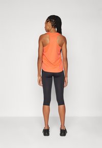 Canotta sportiva arancione con design a racerback, leggings neri alla caviglia e sneakers nere, vista dal retro su uno sfondo neutro.