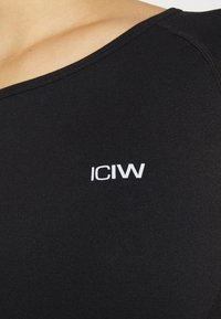 Svart träningslinne i elastiskt material, med rund halsringning och vitt "ICIW"-logotyp på vänster bröst. Slät textur.