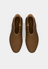 Καφέ δερμάτινα παπούτσια με λεία υφή, στρογγυλή μύτη και μία διακοσμητική λωρίδα. Το εσωτερικό διαθέτει λογότυπο σε χρυσό χρώμα.