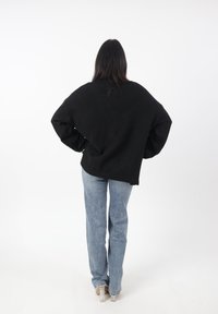 Maglione nero oversize con maniche lunghe, design semplice, texture morbida, indossato con jeans a zampa d'elefante blu chiaro e scarpe con tacco trasparente.