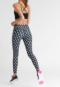 Sujetador deportivo negro con tirantes cruzados en la espalda; leggings negros con lunares blancos; zapatillas negras con detalles en rosa que presentan suelas texturizadas.