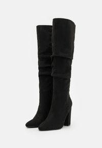 Sorte over-the-knee støvler laget av myk semsket skinn, med en slouchy design, spisse tær og tykke høye hæler.