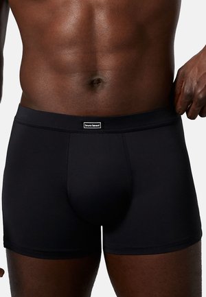 Schwarze Boxershorts aus glattem Stoff mit einem weichen Bund, der ein kleines Logo-Tag trägt. Das Design ist eng anliegend und minimalistisch.