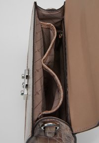 De binnenkant van de handtas met krokodillenprint is voorzien van een beige voering, twee vakken en een ritsvak. Zilverkleurige metalen accenten versieren de sluiting.