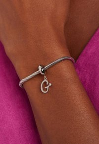 Zilveren armband met een gestructureerde slangenketting, voorzien van een ronde sluiting en een hangende letter "G" bedel met een kleine edelsteenaccent.