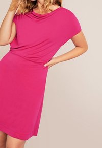 Robe ajustée de couleur rose vif, avec un décolleté drapé, des manches courtes et un ourlet droit. Texture lisse, coupe arrivant au genou.