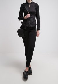 Maglietta nera con zip e colletto rialzato, abbinata a pantaloni neri aderenti e scarpe nere stringate. Design semplice ed elegante. Inclusa borsa a tracolla.