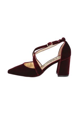 Zapato de tacón alto de terciopelo burdeos con puntera afilada, diseño de tiras cruzadas y tacón ancho. Acentos dorados en el interior visibles.