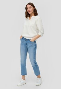 Weißes, strukturiertes V-Ausschnitt-Oberteil mit 3/4-Ärmeln, kombiniert mit hellblauen, cropped Jeans und weißen Sneakern. Einfaches, lässiges Outfit-Design.