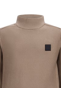 Maglione lavorato a maglia beige con colletto alto, motivo testurizzato e una toppa logo rettangolare nera sul petto.