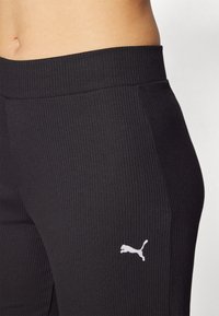 Čierne rebrované legíny s bielym logom Puma. Pás je hladký a elastický, čo zabezpečuje pohodlné priliehavé nosenie pri aktívnych činnostiach.